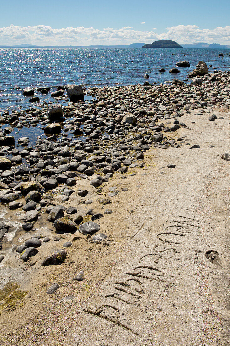 Neuseeland ist im Sand geschrieben, man blickt auf den Lake Taupo an der Five Mile Bay, nahe Waitahanui, Waikato, Nordinsel, Neuseeland