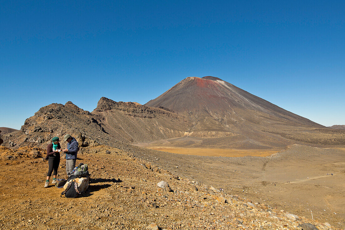 Two hikers at the flat bottom of the South Crater of the active volcano Mount Ngauruhoe, one of the Great Walks of New Zealand, Tongariro National Park, North Island, New Zealand