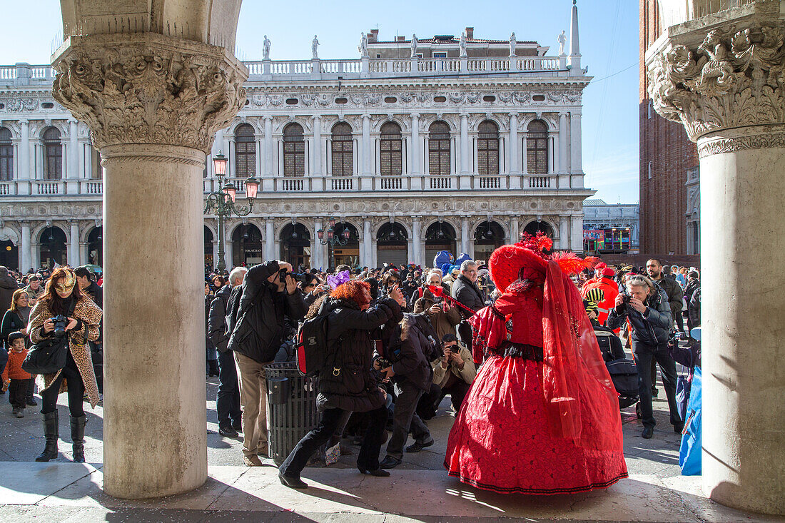 Venetian Carnival, tourism, masks, red dress, costume, posing, army of  photographers, arcade of Doge Palace, San Marco, Venice, Italy