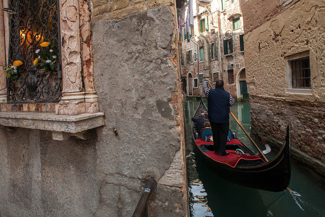 tourist trip on gondola in a narrow canal in historic Castello, rowing gondolier, shrine of the Virgin Mary, romantic, old walls, Venice, Veneto, Italy