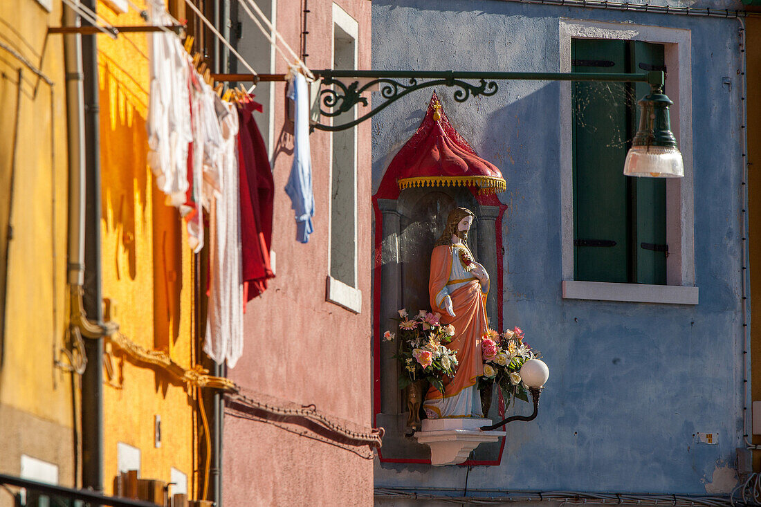 Jesus-Schrein mit Blumenschmuck an bunter Hausfassade, Fischerinsel Burano, Venedig, Italien