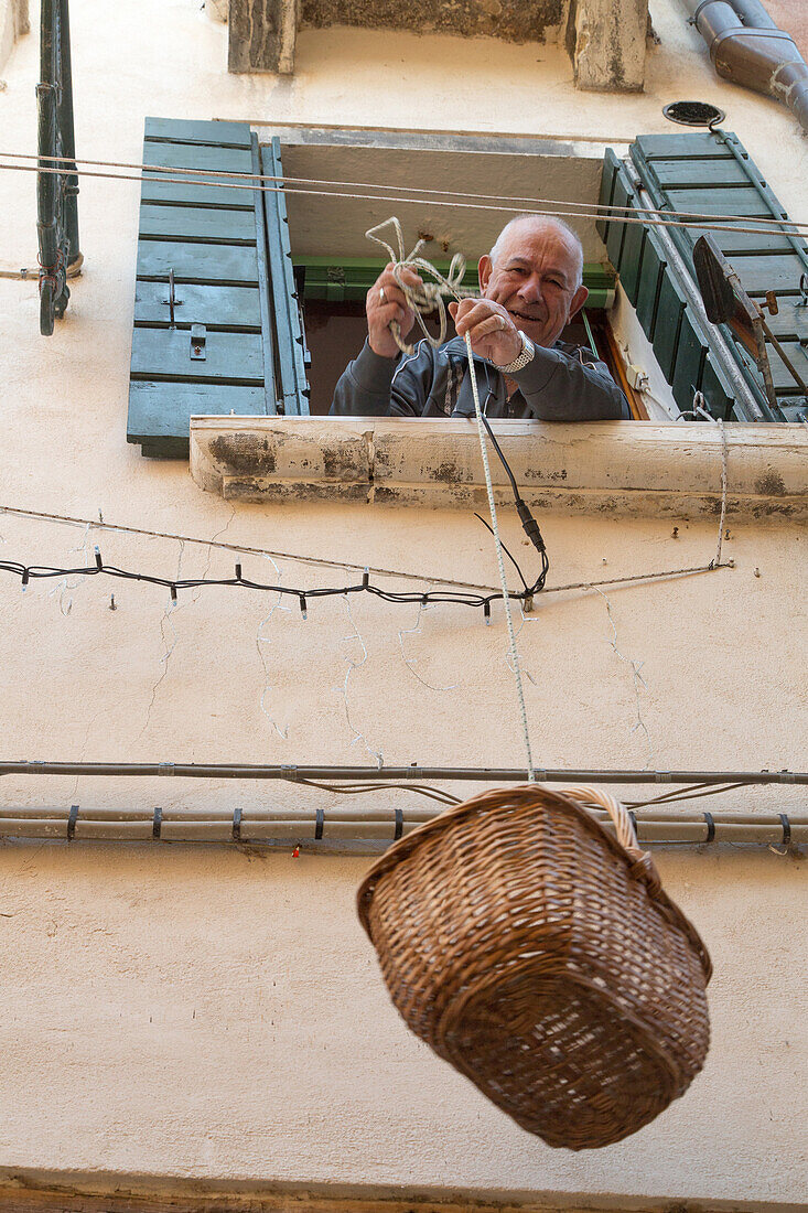 Briefträgerin und älterer Herr, zieht Weidenkorb mit seiner Post nach oben, Venedig, Italien