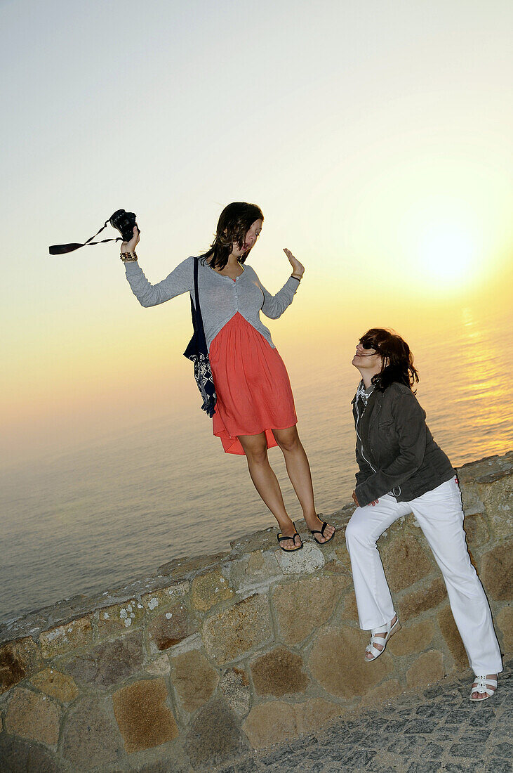 Two women taking photographs at the coast at sunset, Cabo da Roca, West coast near Lisbon, Portugal