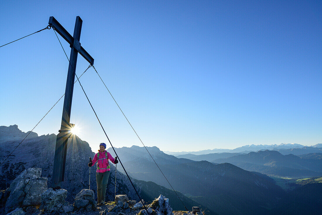 Woman reaching cross Heimkehrerkreuz beneath summit of Ulrichshorn while hiking, Nurracher Hoehenweg, Ulrichshorn, Loferer Steinberge range, Tyrol, Austria