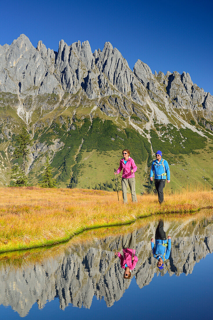 Man and woman hiking near a mountain lake with Mandlwand ridge at Hochkoenig in the background, Berchtesgaden range, Salzburg, Austria