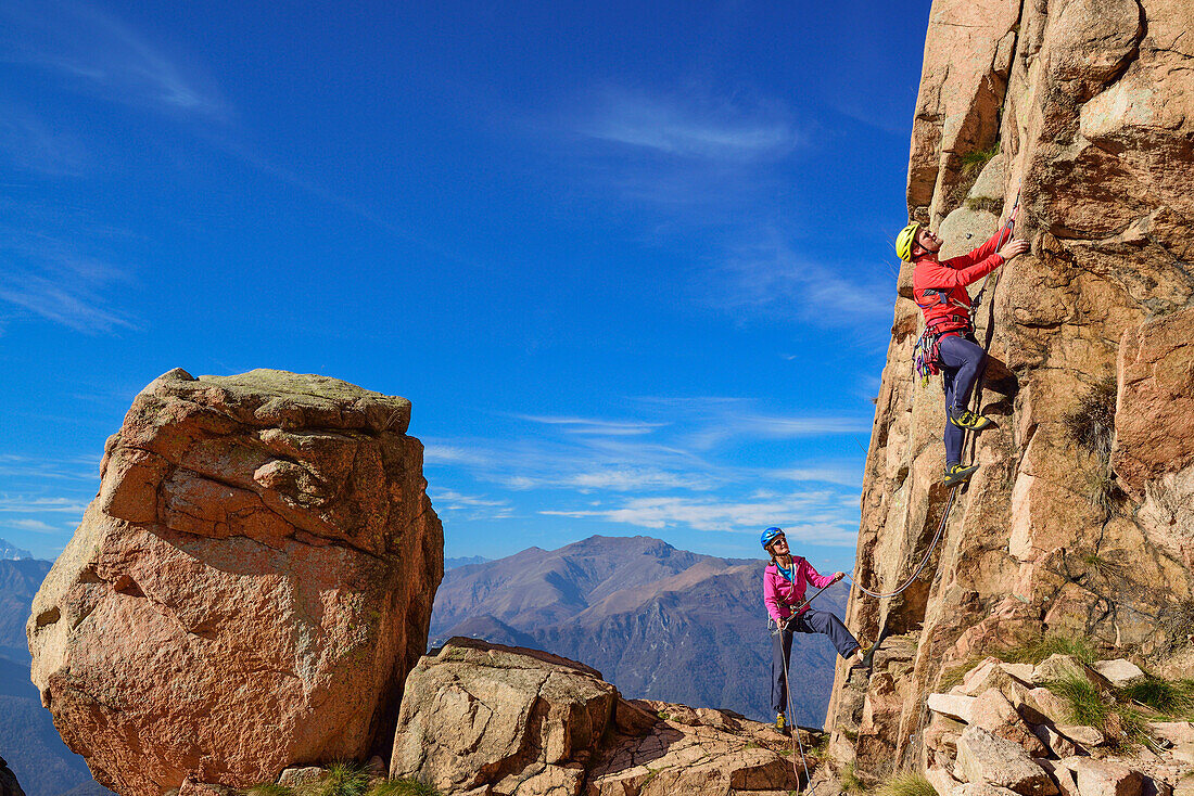 Man climbing on red Granite rock is being belayed by woman, Mottarone, Piedmont, Italy