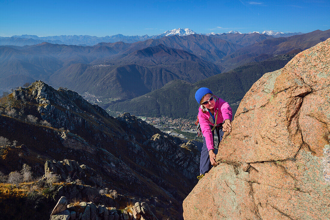 Woman climbing on red Granite rock with view to Monte Rosa in Valais, Mottarone, Piedmont, Italy