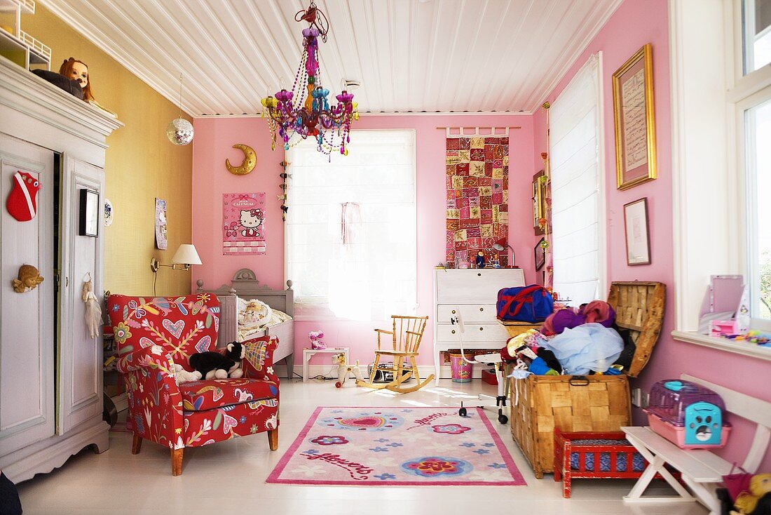 A child's room with white wooden ceiling, a reading chair and a toy box in front of a coloured wall