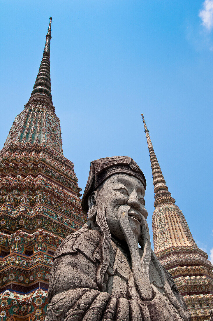 'Stone guard statue and temple spires (chedi) at Wat Pho, the Temple of the Reclining Buddha, the largest Buddhist temple in Bangkok; Bangkok, Thailand'
