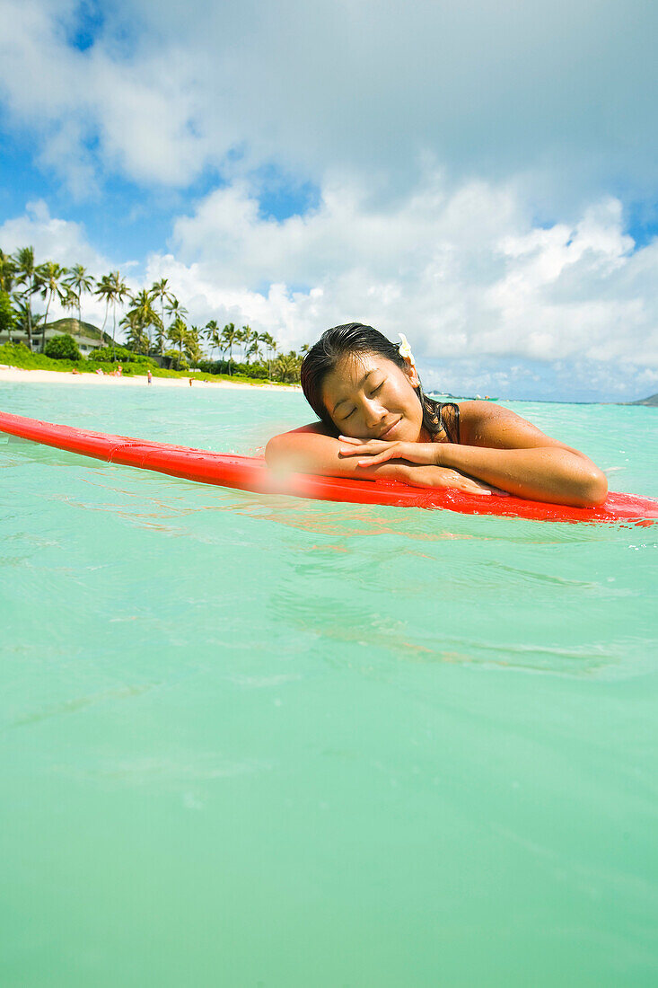 Hawaii, Oahu, Lanikai, Junge japanische Frau auf Surfbrett im Ozean liegend.