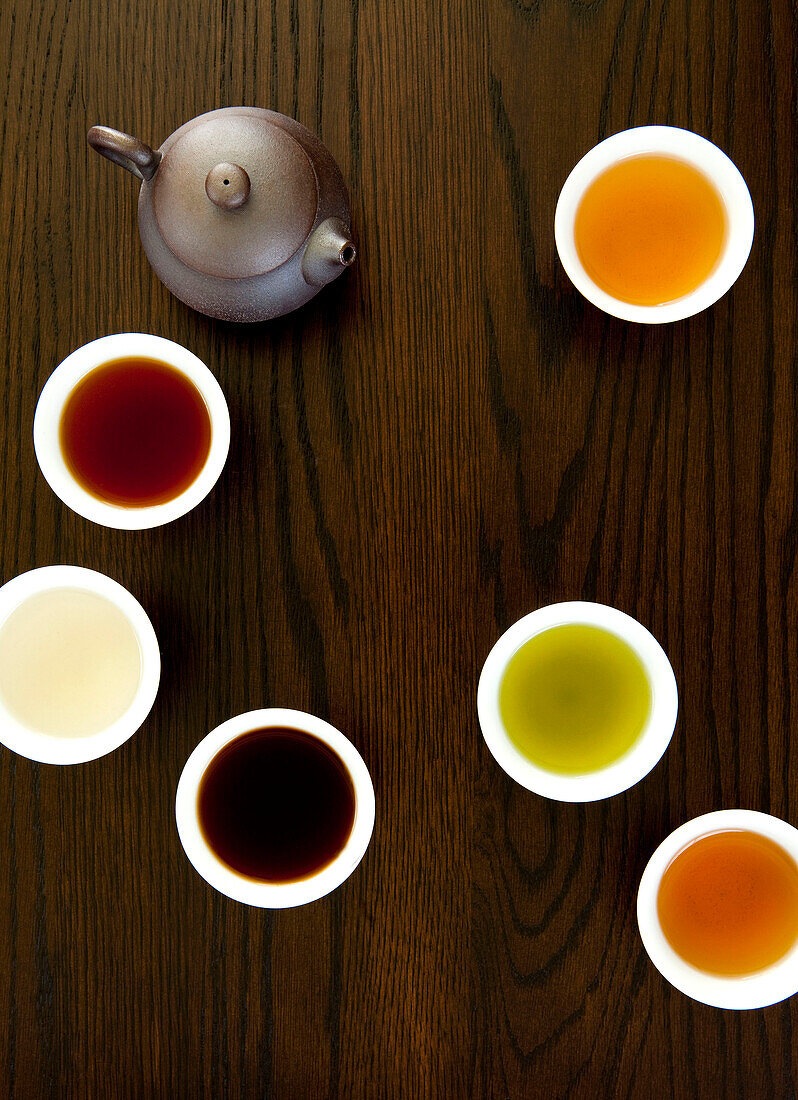 Teapot And Different Types Of Tea In Cups On A Wood Table