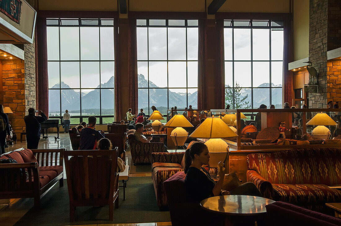 'Jackson Lake Lodge, guests in lobby with storm brewing outside, view at Teton Mountains; Wyoming, United States of America'