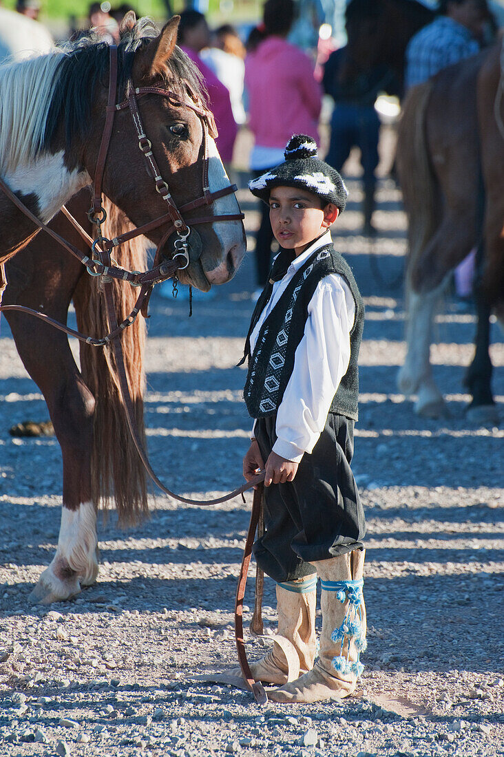 'A young boy dressed in traditional costume stands by a horse; Malargue, Argentina'