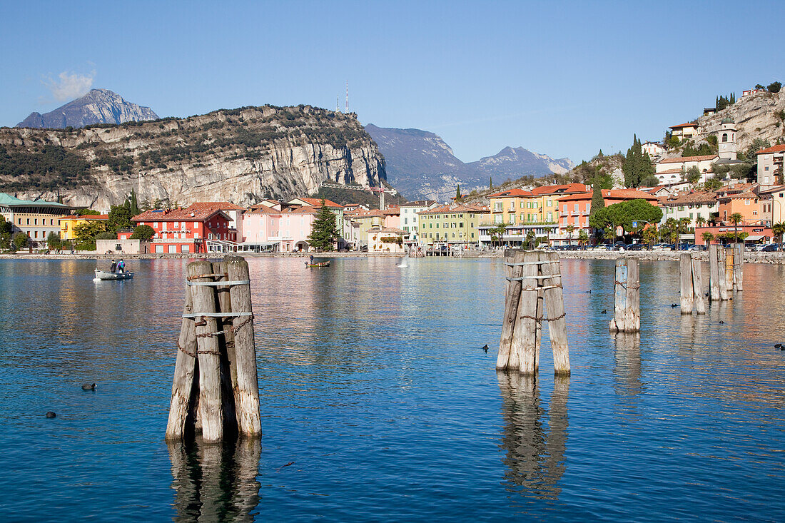 'Wooden pilings in the water in Lake Garda with buildings along the water's edge; Malcesine, Verona, Italy'
