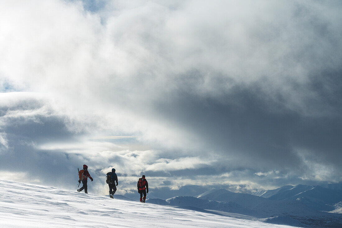 'Three walkers on snowy, winter walk ascending Geal Charn, near Laggan; Scotland'