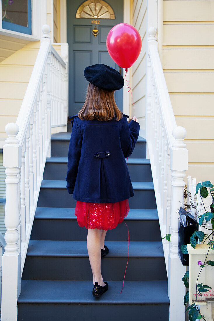 'A young girl is walking up the stairs of a house with a balloon; San Francisco, California, USA'