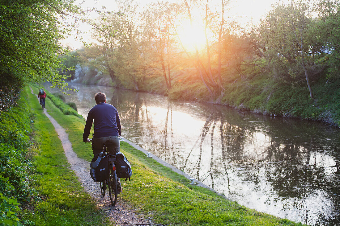 'Cyclist cycling along canal side at sunset; Wiltshire, England'