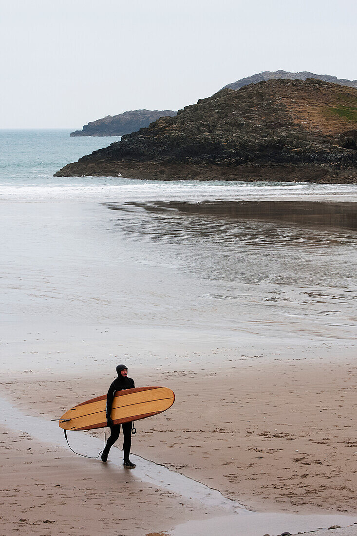 'Surfer coming out of the chilly winter waters heading to car park at Whitesands Beach on the Pembrokeshire Coast Path; Pembrokeshire, Wales'