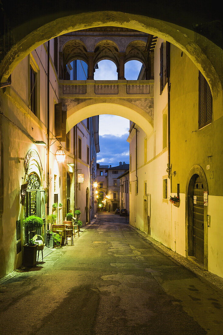 'Street between residential buildings illuminated with lights at dusk; Spoleto, Umbria, Italy'