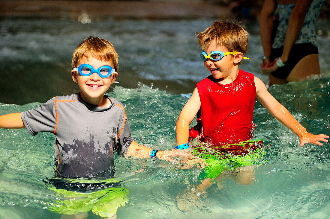 Two boys playing in a swimming pool with goggles on.