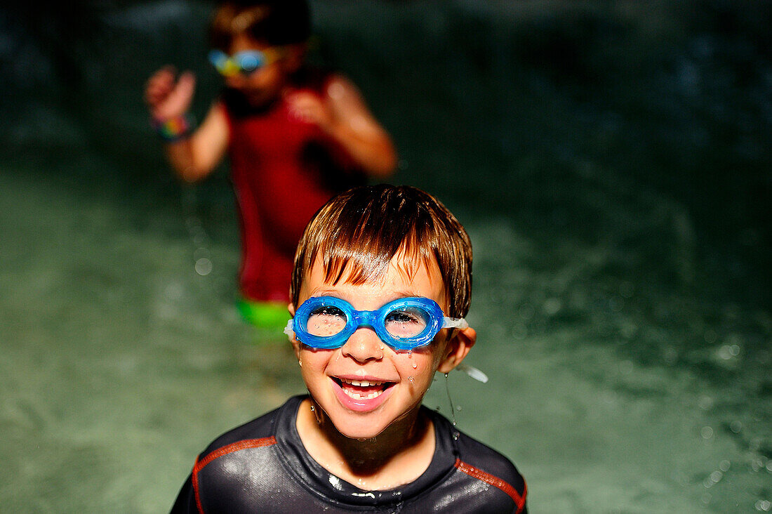 Young boy smiling with goggles in a swimming pool.