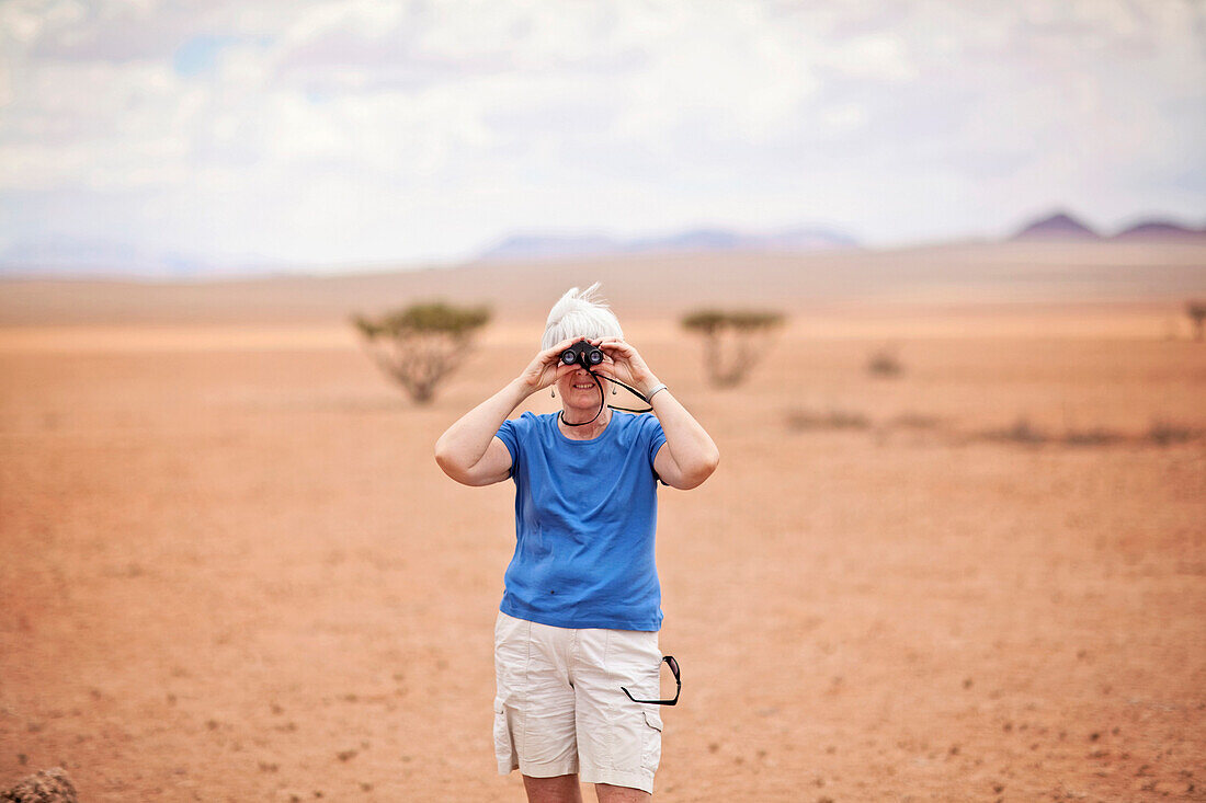 An older woman looks through binoculars while on safari in the Namib Desert, Namibia