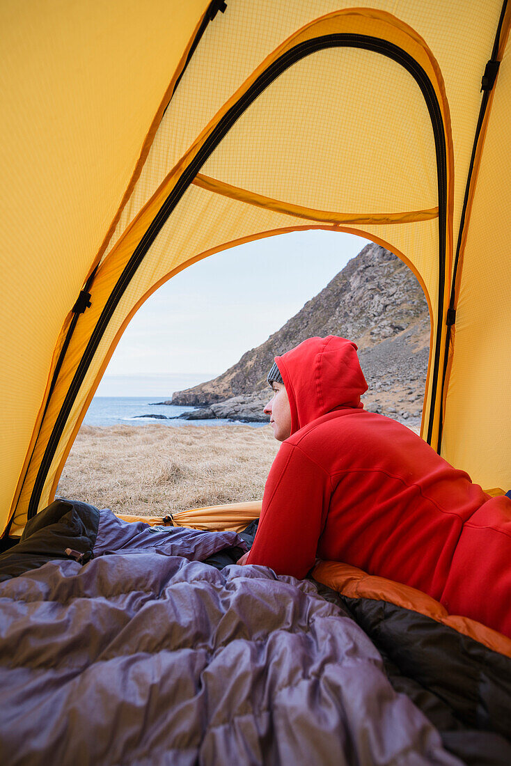 Female backpacker looks out of tent while wild camping at Horseid beach, Moskenes??y, Lofoten Islands, Norway