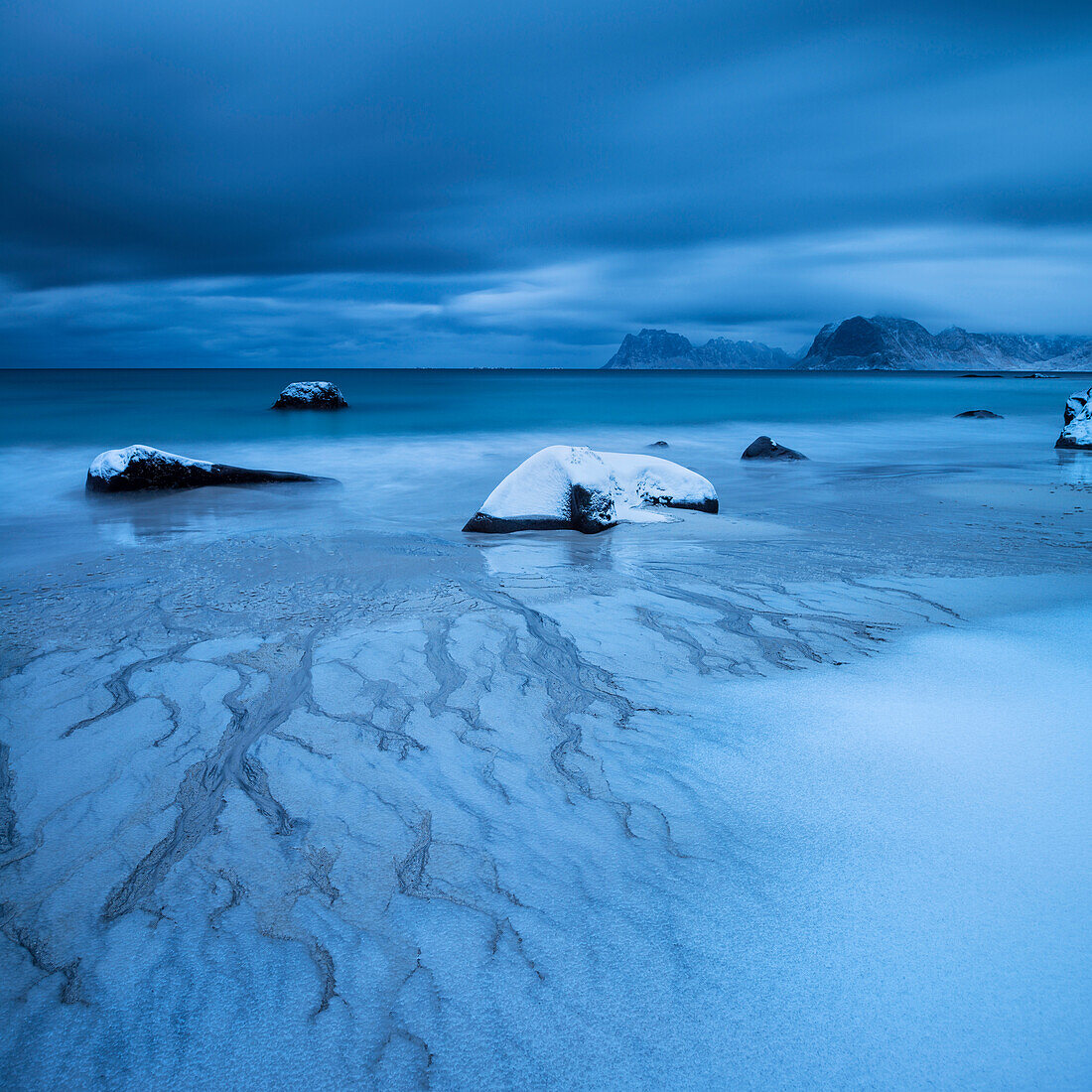 Waves wash over snow covered sand in winter at Myrland beach, Flakstad??y, Lofoten Islands, Norway