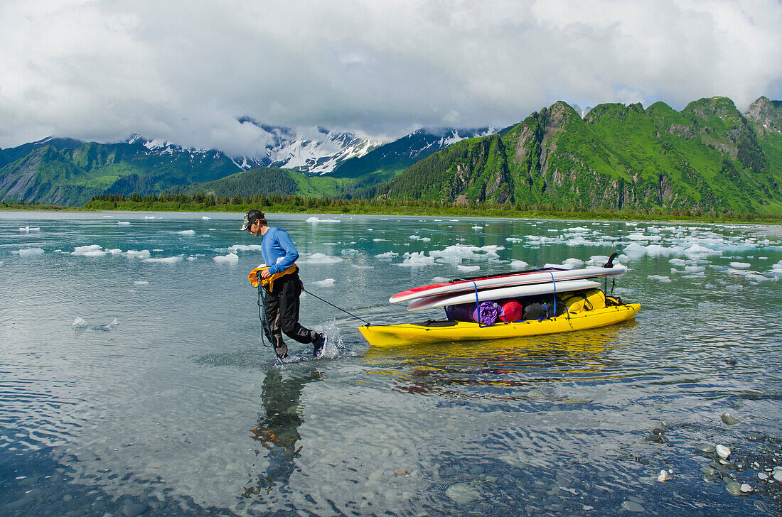 Man hauls SUPs and gear on a kayak up the feeder river to Bear Lake and Bear Glacier, Alaska.
