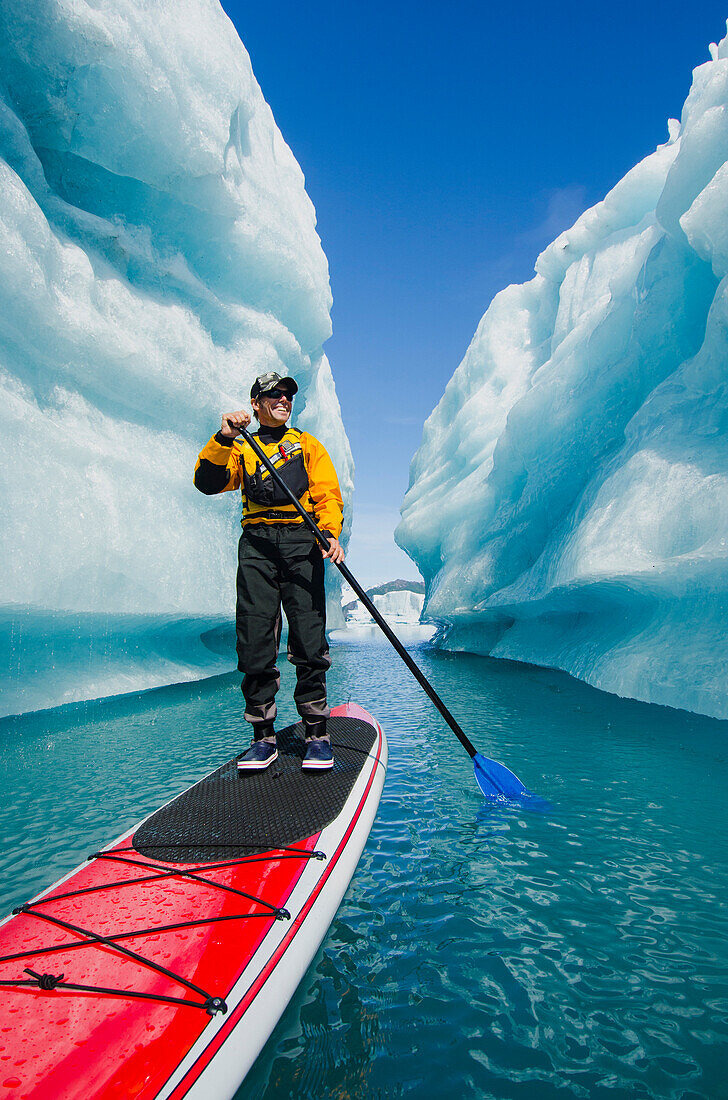 A man on stand up paddle board (SUP) explores an iceberg canyon on Bear Lake in Kenai Fjords National Park, Alaska.