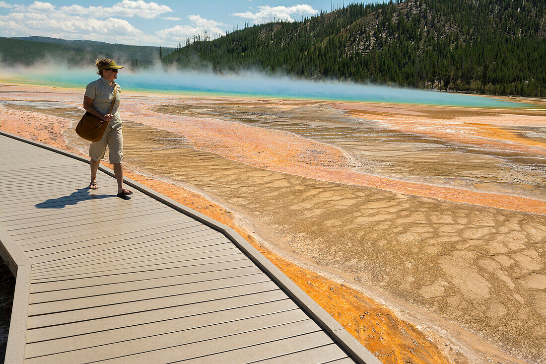 A woman hiking along the boardwalk next to the Grand Prismatic Springs , a thermal hot spring in  Yellowstone National Park, Wyoming.