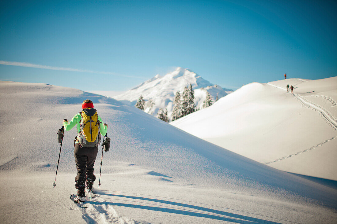 A female snowshoer walks a ridgeline with Mount Baker in the background.