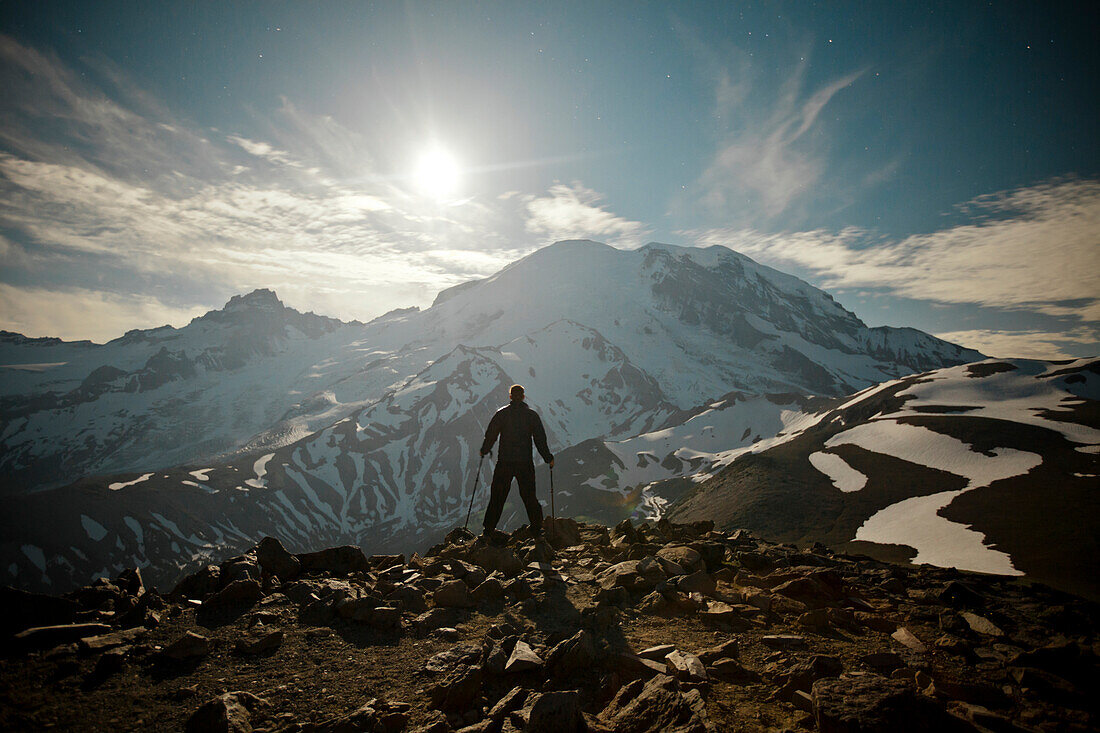 A hiker stands on Burroughs Mountain while the Moon rises over Mount Ranier.