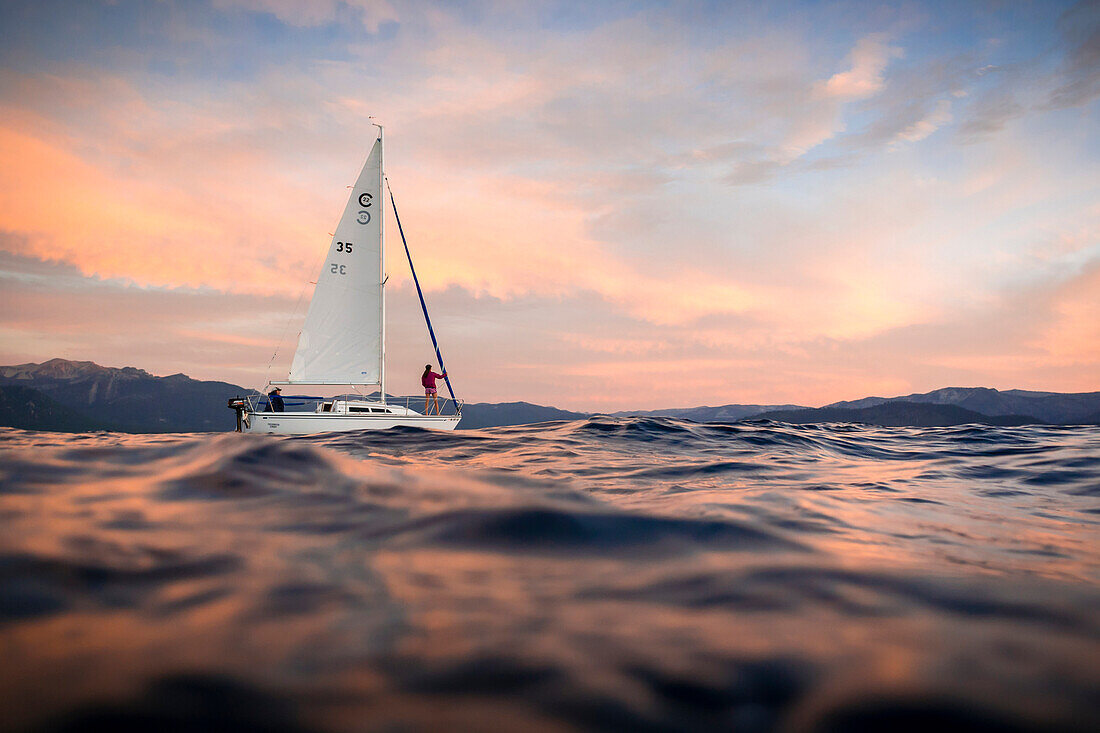 Clint Celio (skipper) and Sabina Allemann (crew) sail the small yacht Freshwater Cowboy on Lake Tahoe at sunset.