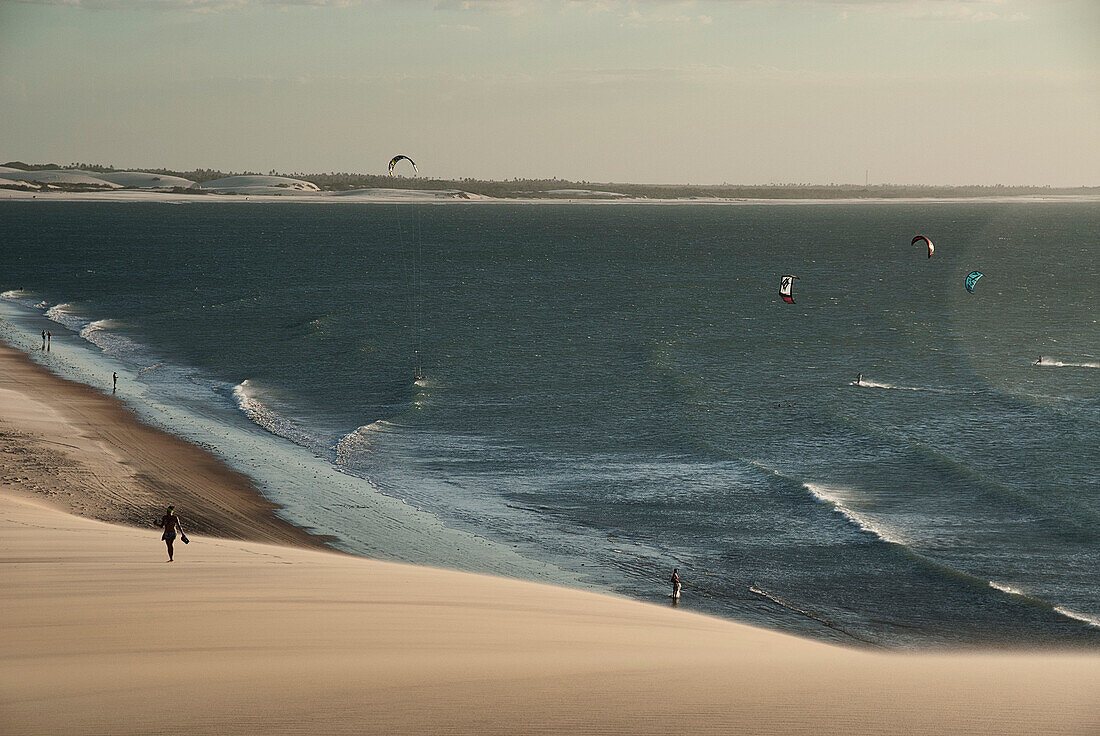 Girl in silhouette walking by dunes of Jericoacoara with a sea full of people kiteboarding in Brasil