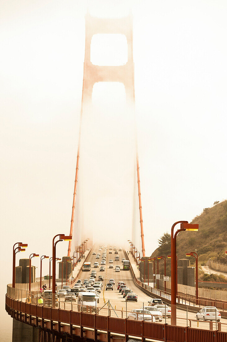 Front view of the Golden Gate with pedestrian and automobile traffic surrounded by fog.