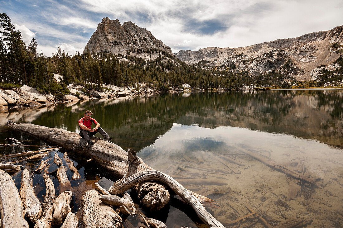 Boy sitting on a tree trunk at the edge of a mountain lake in Mammoth Lakes, California.