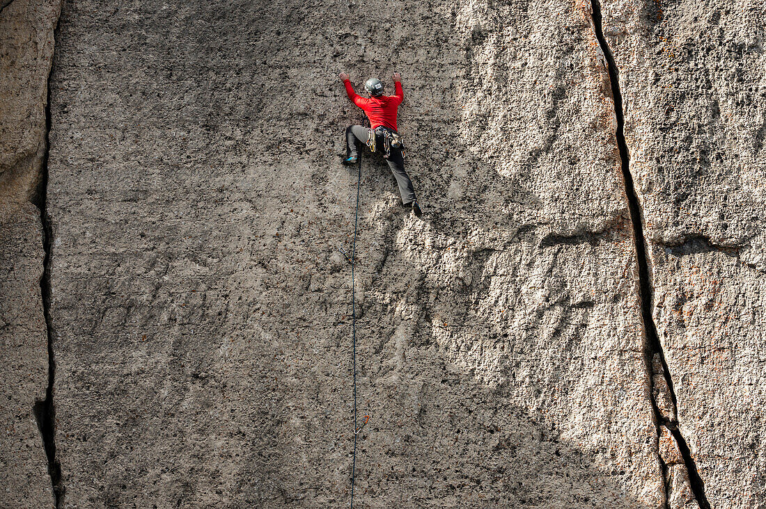 Man with red jacket, grey helmet and various climbing gear climbing a wall above Teton Village, near Corbet's Couloir, Jackson Hole, Wyoming.