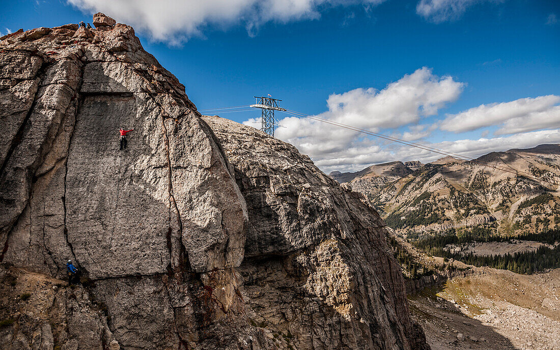 Two climbers while climbing a crag in Jackson Hole with the cable car cables and pylon in background. Teton Village, Wyoming.