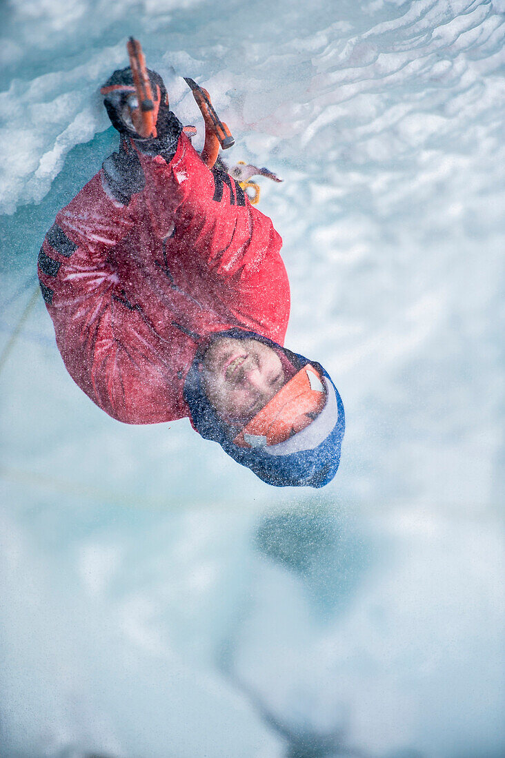 Man with red jacket and orange helmet and ice axes lead climbing an ice fall in the middle of a snow storm in Simplon Pass shooted from above. Valais, Switzerland.