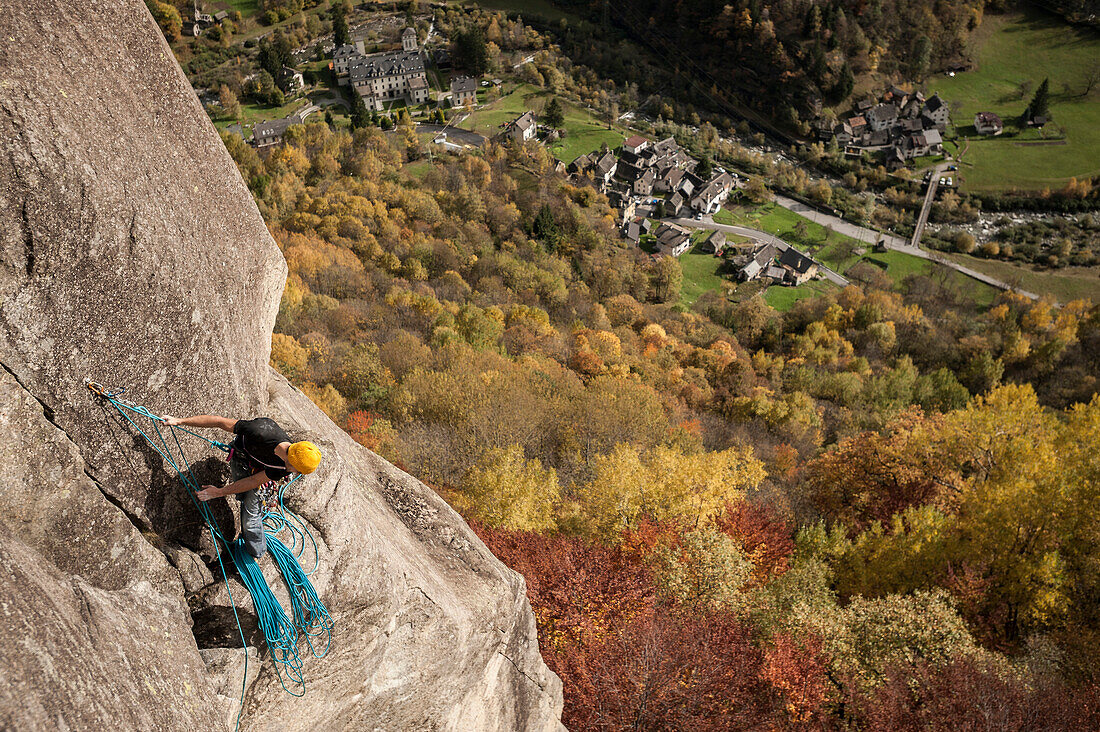 Climber belaying his partner from the top of a pitch in Cadarese with the village and the valley in background. Ossola, Italy.
