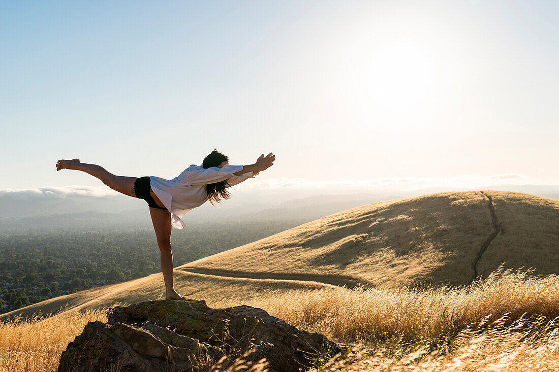 Woman in yoga pose in a field of golden grass in sun drenched hills of California.