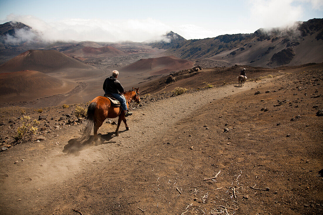 Two men on horseback ride into Haleakala crater.