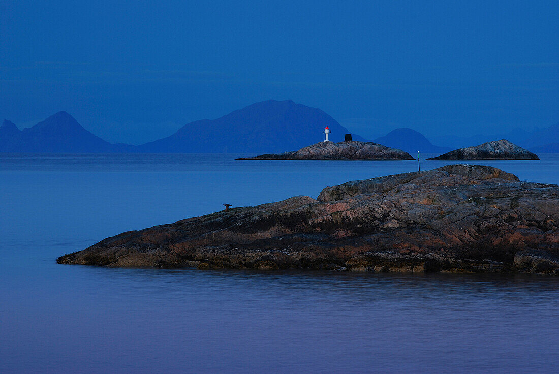 Lighthouse on small rock island at night.