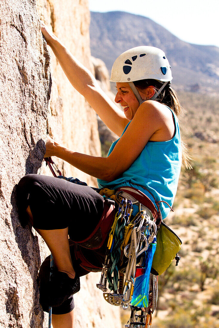 A female climber adjust a spring loaded camming device while working her way up Sidewinder (5.10b) in Joshua Tree National Park, California.