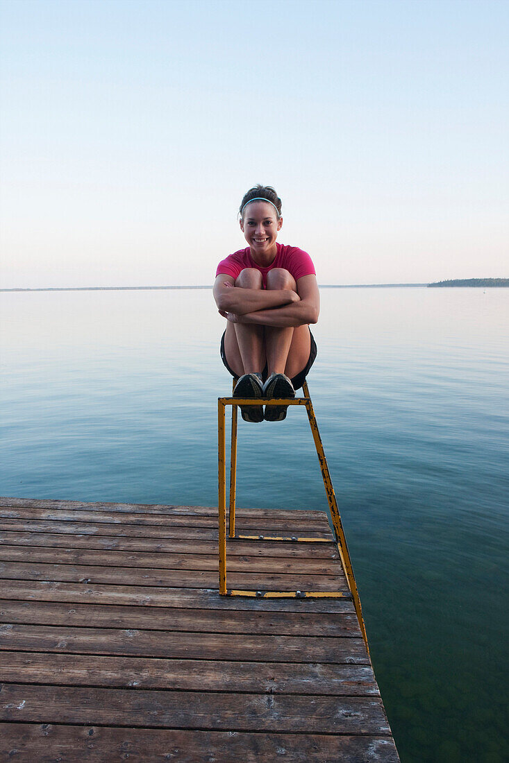 Young Woman Seated On Dock Ladder, Clear Lake, Riding Mountain National Park, Mantioba, Canada