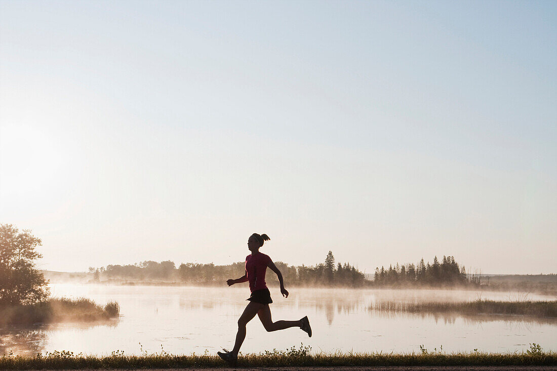 Silohuette Of Woman Running By Lakeshore, Clear Lake, Riding Mountain National Park, Manitoba, Canada