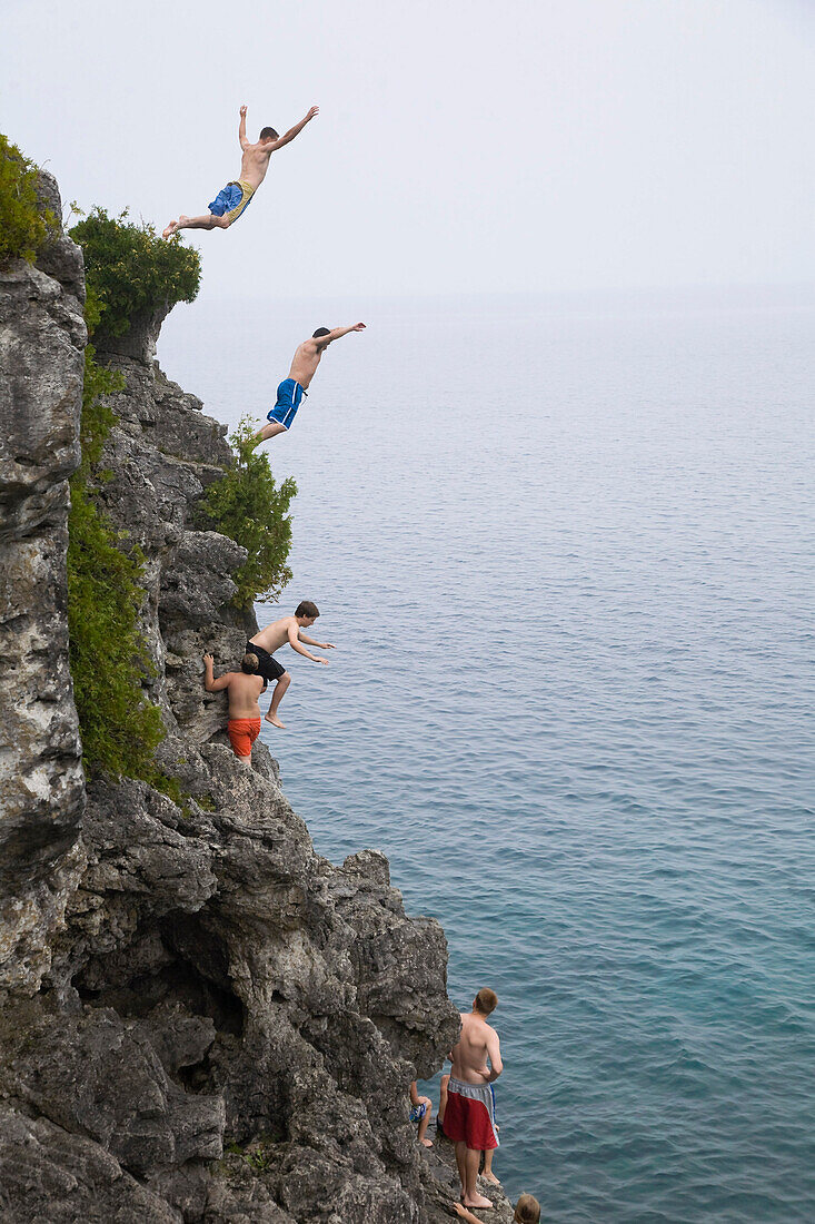 'Men leaping from a cliff into turquoise water of Georgian Bay in Bruce Peninsula National Park; Ontario, Canada'