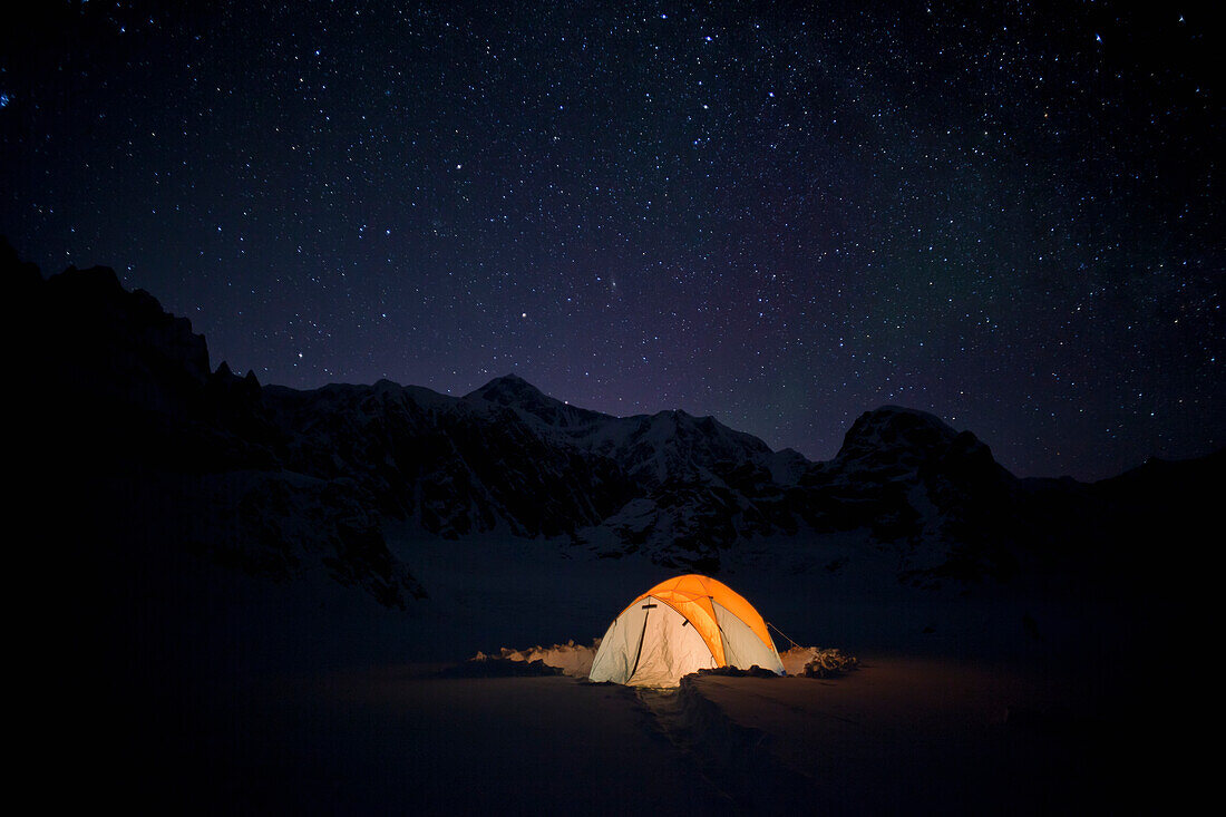 'Mountain tent on Ruth Glacier at night under star studded sky, illuminated by head lamp with the summit of Mt. McKinley in background, Denali National Park and Preserve; Alaska, United States of America'