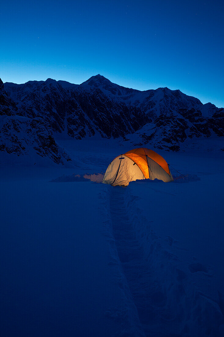 'Mountain tent on Ruth Glacier in evening, illuminated by head lamp with the summit of Mt. McKinley in background, Denali National Park and Preserve; Alaska, United States of America'